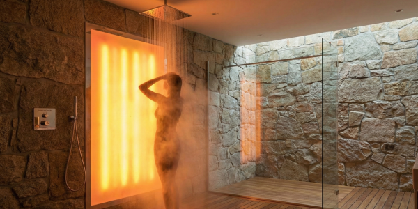 Silhouet van een persoon die doucht in een moderne badkamer met stenen muren en een groot, warm oranje lichtpaneel dat achter hen schijnt.